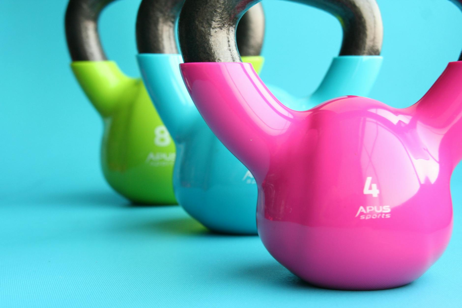 green blue and pink kettle bells on blue surface